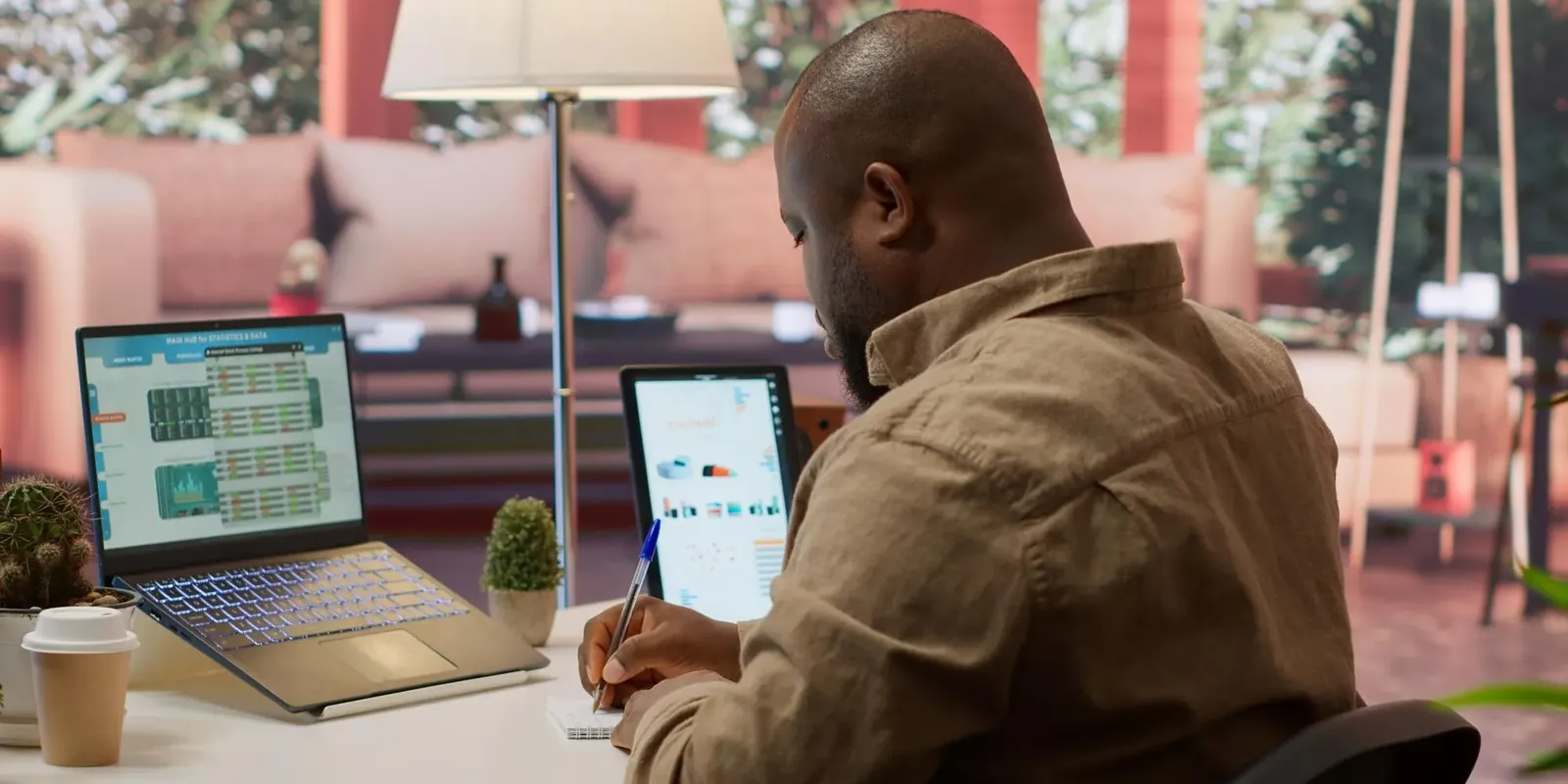 Black entrepreneur at his desk taking notes in front of a laptop and a tablet showing his performance metrics